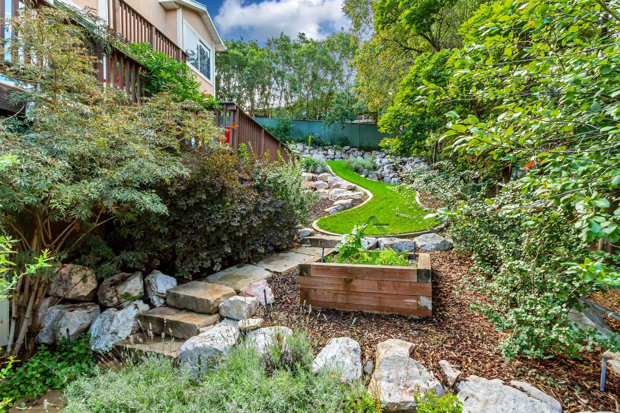 Tiered outdoor space with a wooden deck, stone steps, raised planter box, and artificial turf landscaping