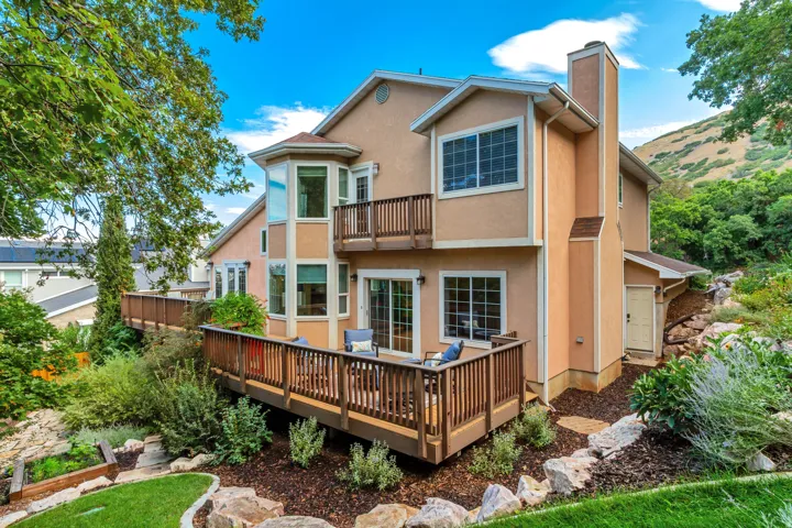 Multi-level wooden decks with baluster railings, stucco exterior, multiple large windows, and a prominent chimney feature