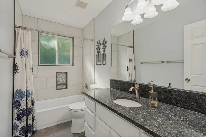 Bathroom featuring a dark speckled countertop, white cabinetry, undermount sink, and a framed mirror