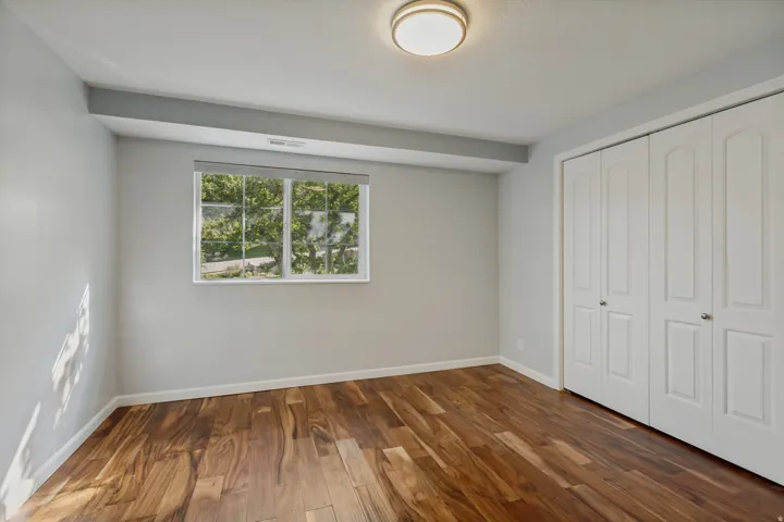 Wood-finish flooring, white bi-fold closet doors, white window trim, and a flush-mount ceiling light