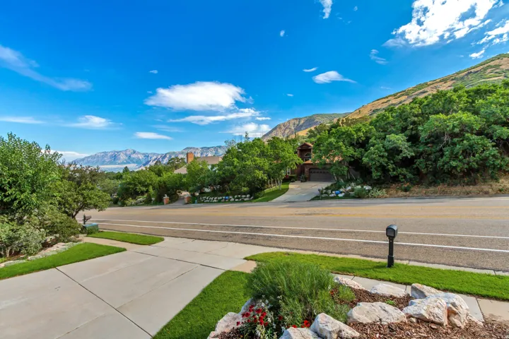 Concrete driveway with manicured lawn and mature landscaping, complemented by a prominent mountain backdrop