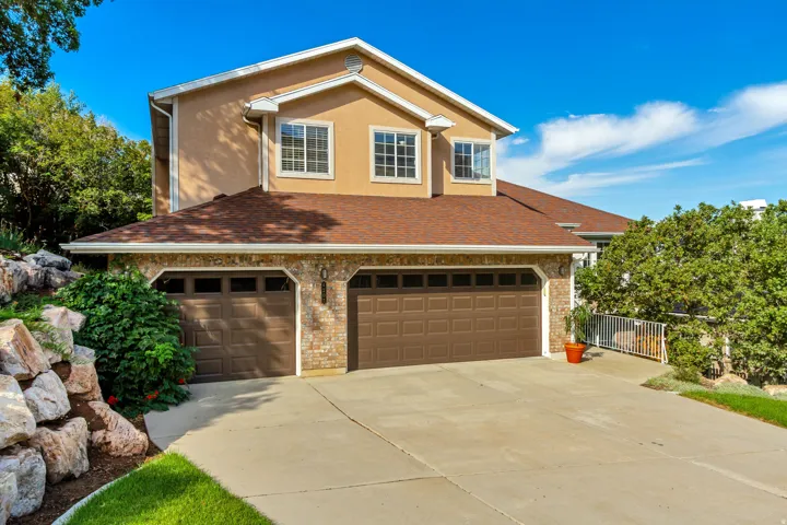 Two-story stucco and brick exterior with a multi-car garage, concrete driveway, and mature landscaping