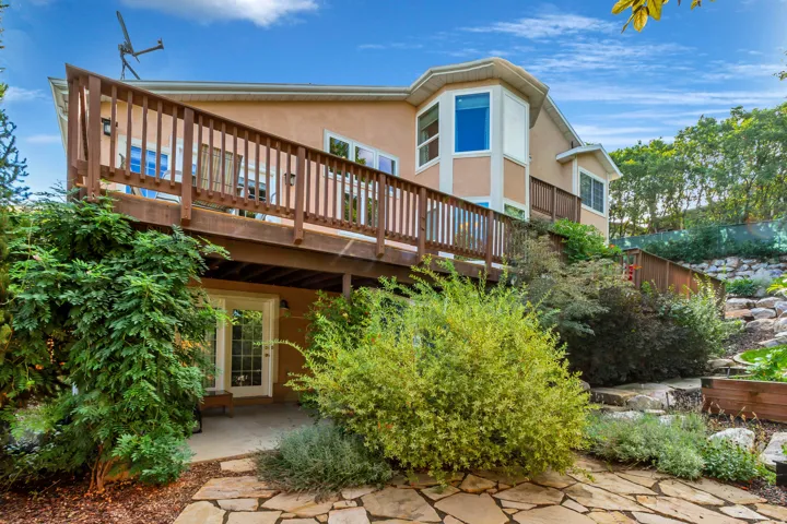 Multi-level outdoor living featuring an expansive wooden deck, stone patio, and landscaped terraced garden beds