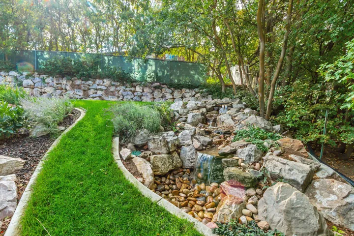 Tiered rock wall landscaping with an integrated waterfall feature, a meandering grass pathway, and established trees