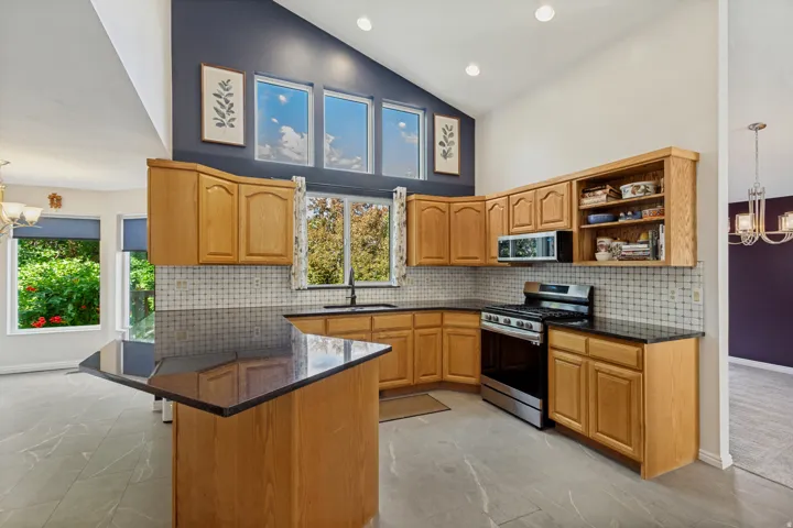 Kitchen featuring vaulted ceilings, light wood cabinetry, dark countertops, a stainless steel range, and tile flooring