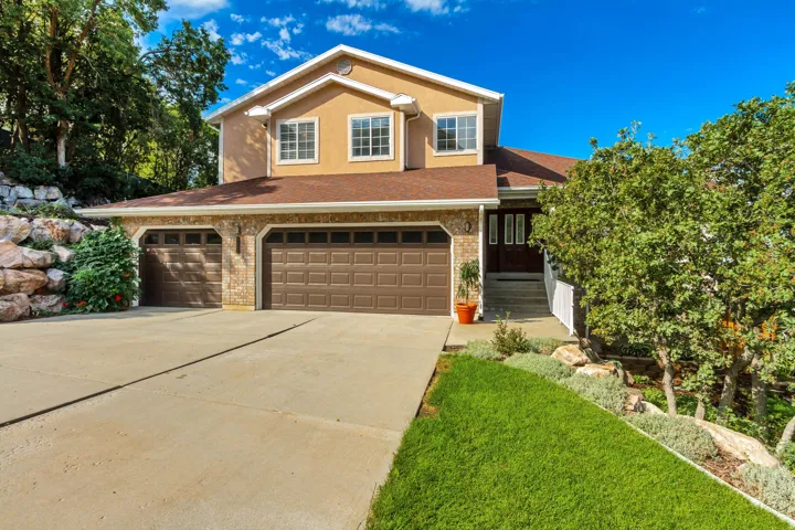 Multi-story residence featuring a two-car garage with panel doors, a stone veneer and stucco exterior, and a concrete driveway