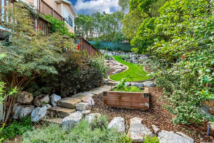 Tiered outdoor space with a wooden deck, stone steps, raised planter box, and artificial turf landscaping