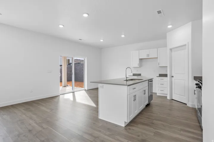 Open-concept living space with wood-finish flooring, recessed lighting, and a white kitchen with shaker cabinets