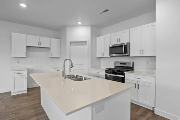 Kitchen featuring white cabinetry, light-toned countertops, stainless steel appliances, a center island with an undermount sink, and wood-finish flooring