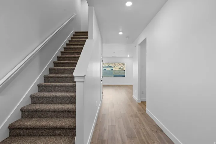 Carpeted staircase with white handrail, recessed lighting, and wood-finish flooring
