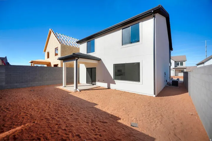 White stucco exterior with black-framed windows, a covered patio, and a concrete block perimeter wall