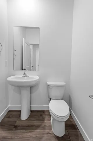 Pedestal sink with chrome faucet, wall-mounted mirror, white toilet, and wood-finish flooring