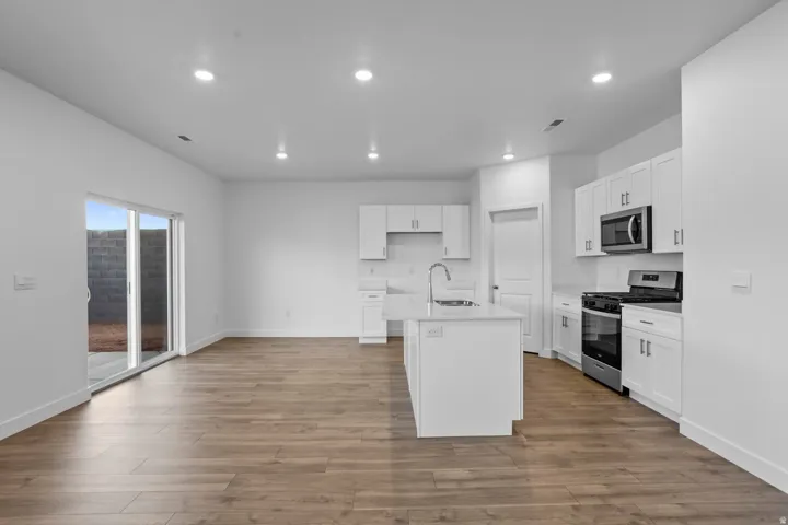 White cabinetry, stainless steel appliances, wood-finish flooring, recessed lighting, and a kitchen island with a sink