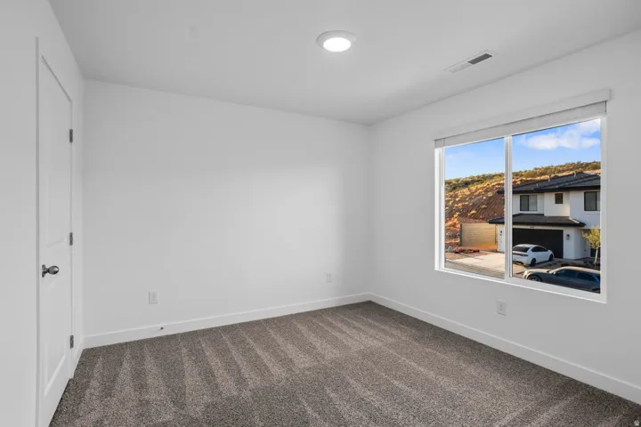 Recessed ceiling lighting, white interior door with black hardware, neutral wall paint, carpeted flooring, and a large window with roller shades