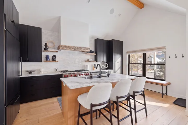 Vaulted ceiling with exposed wood beam, black cabinetry, stone countertops, integrated range, and a large window