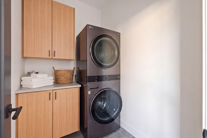 Built-in stacked washer and dryer, light wood-finish cabinetry, light countertop, and dark hardware