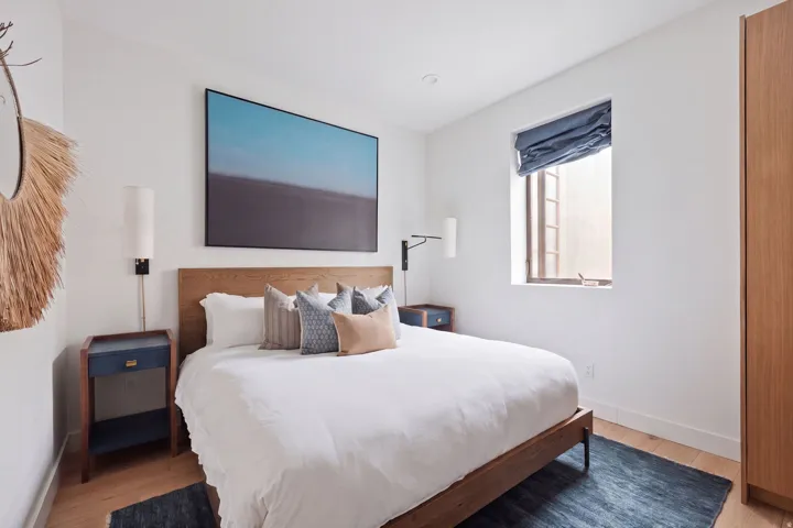 Recessed ceiling lighting, wood-finish flooring, built-in wardrobe, natural wood headboard, and a window with a fabric shade