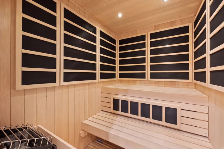 Dedicated sauna room featuring light wood paneling, built-in multi-level bench seating, integrated heating elements, and recessed ceiling lighting
