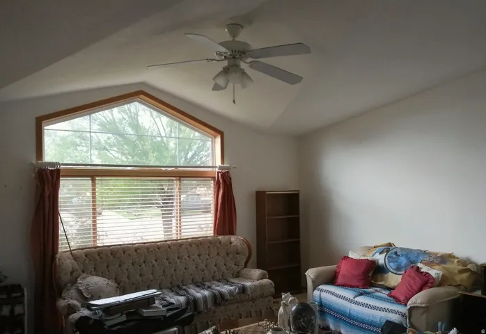 Vaulted ceiling, oversized triangular window, wood-finish window trim, ceiling fan light fixture, white wall finishes