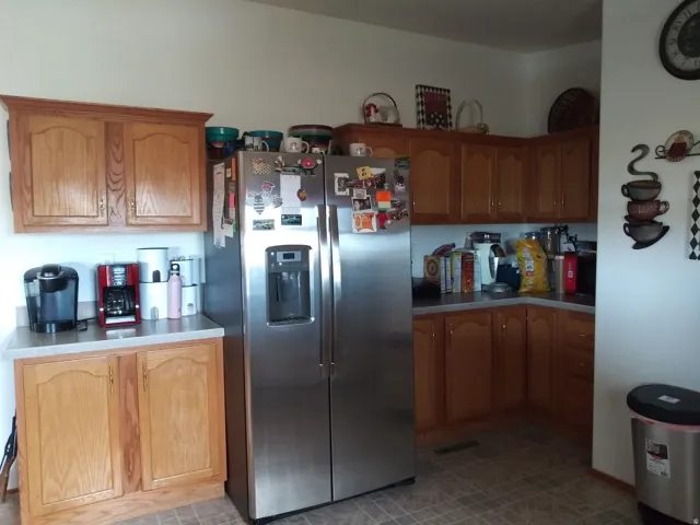 Stainless steel side-by-side refrigerator, wood-finish cabinetry, light-toned countertops, and mosaic-style floor tiles