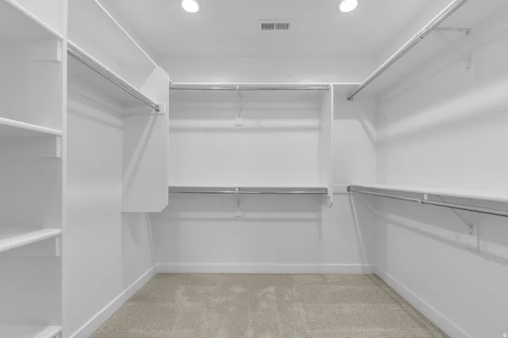 Walk-in closet featuring white built-in shelving, chrome hanging rods, recessed lighting, and carpet flooring
