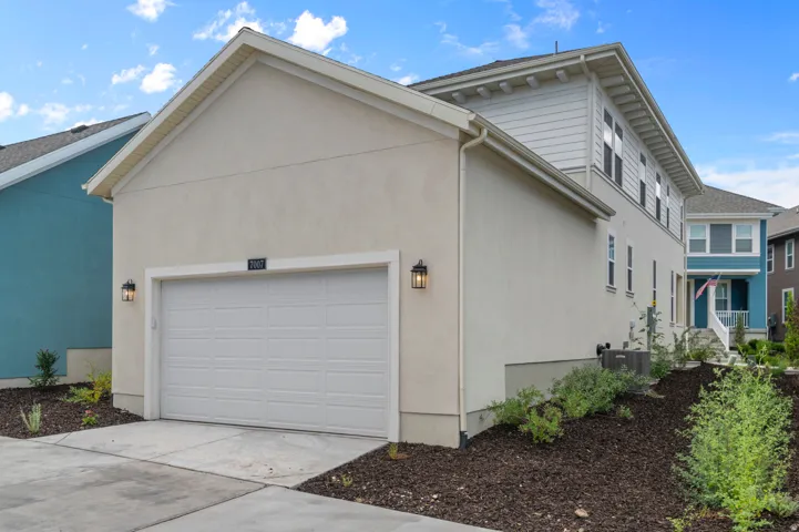 Stucco exterior featuring a two-car garage with a panel door, modern exterior lighting, and minimal landscaping
