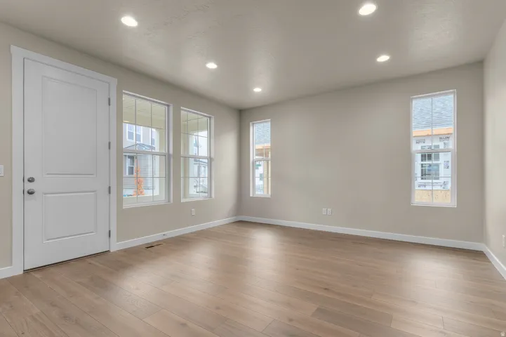 Recessed lighting, wood-finish flooring, multiple windows, white trim, and a paneled entry door