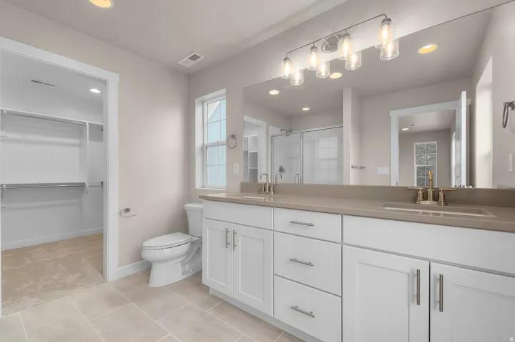 Dual sink vanity with white cabinetry and a light-toned countertop, large wall-mounted mirror, and tile flooring