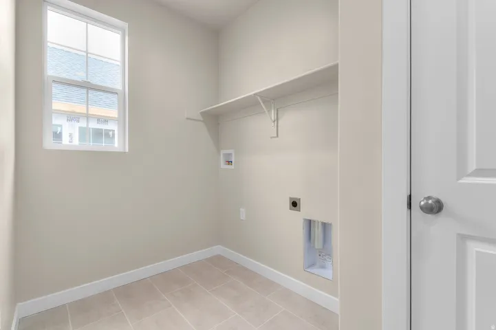 Utility room featuring a window, tile flooring, wall shelving, and laundry hookups