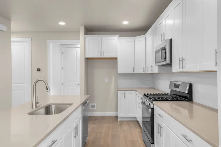Kitchen featuring white shaker cabinetry, light-toned countertops, stainless steel appliances, and wood-finish flooring