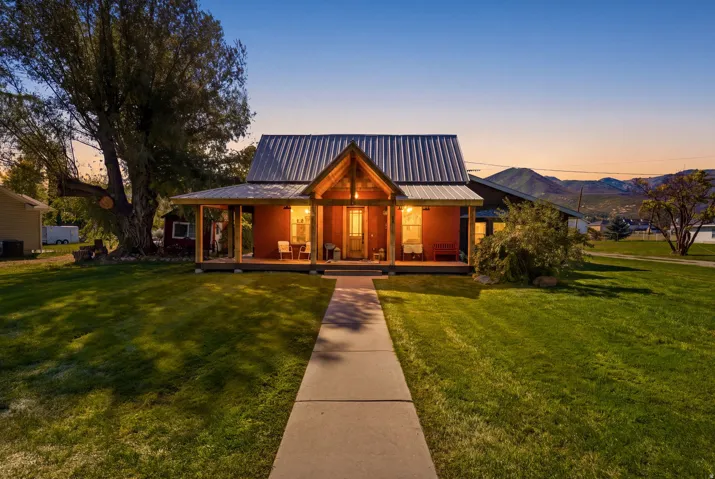 Front exterior featuring a covered porch with exposed wood beams, a metal roof, and a mature tree