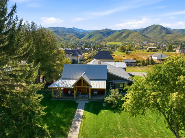 Expansive green lawn, mature trees, covered front porch, and a light-colored metal roof