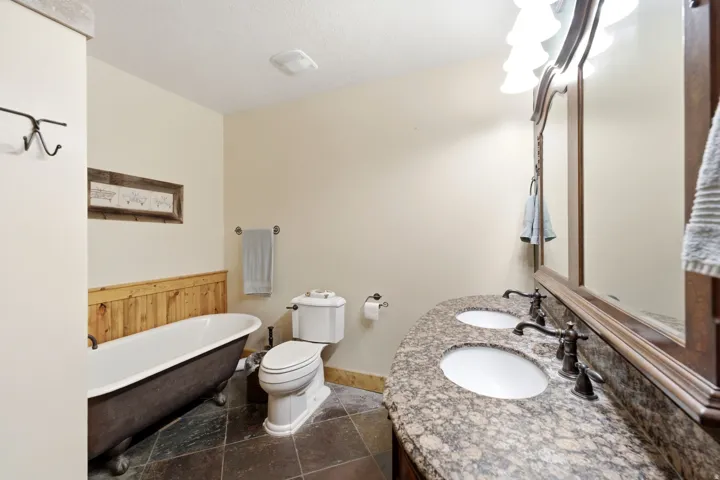 Bathroom featuring a dual vanity with a granite countertop, undermount sinks, bronze-finish fixtures, a clawfoot tub, and wood paneling
