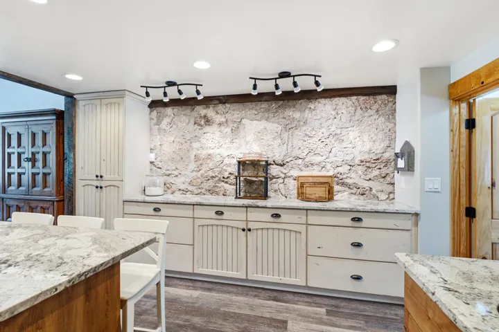 Exposed stone wall, track lighting, wood-finish flooring, recessed ceiling lights, and light-toned cabinetry with dark hardware