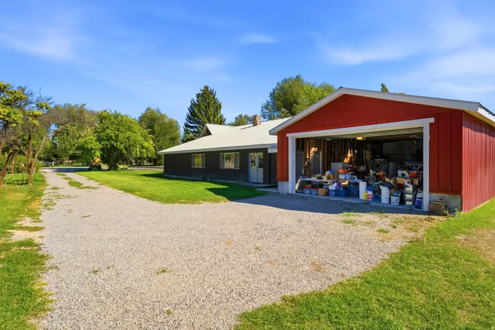 Gravel driveway, expansive green lawn, mature trees, red attached garage, additional property structure
