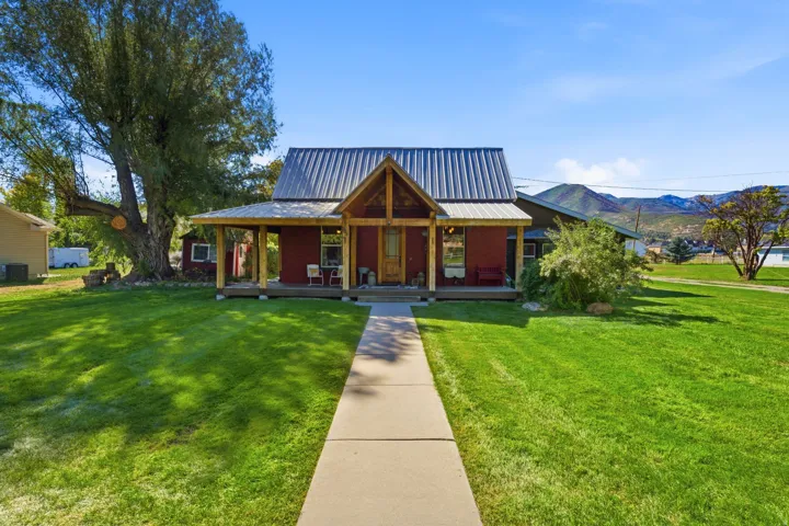 Red exterior residence featuring a covered front porch, metal roof, and wood accents