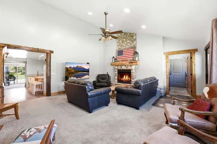 Stone-clad fireplace with wood mantle, vaulted ceiling with recessed lighting, and a ceiling fan