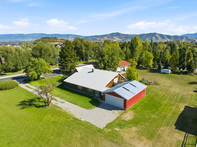 Expansive property featuring a ached red barn-style garage, gravel driveway, and mature trees