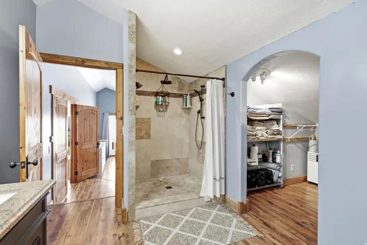 Tiled shower with a curtain rod and multiple shower heads, wood-finish flooring, vaulted ceiling, and an arched doorway