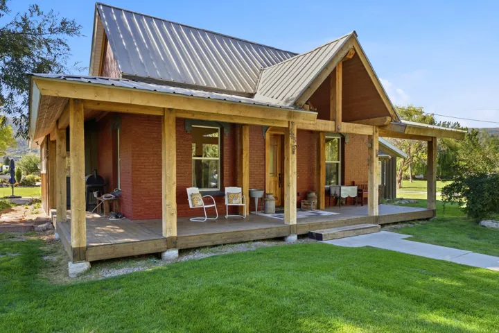 Red brick exterior with a wrap-around porch, wood posts, and a metal roof