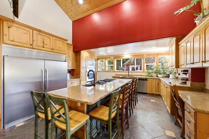 Kitchen featuring vaulted wood-paneled ceilings, natural wood cabinetry, stainless steel appliances, a large island with a cooktop, and stone tile flooring