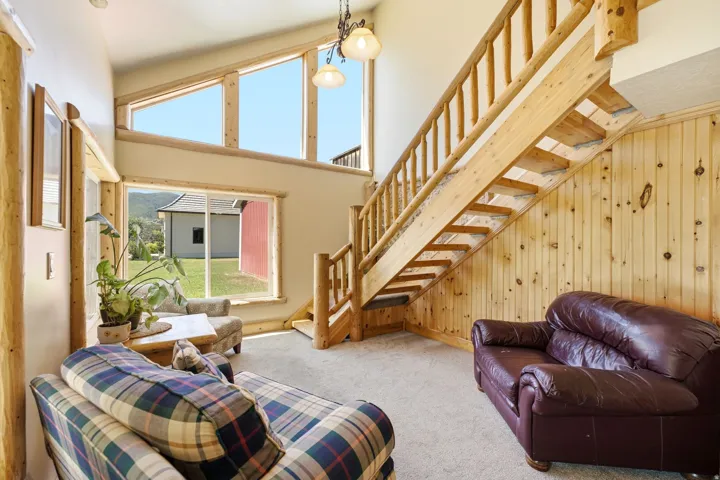 Vaulted ceiling with exposed wood-finish beams, natural wood staircase, wood-paneled wall, and large windows