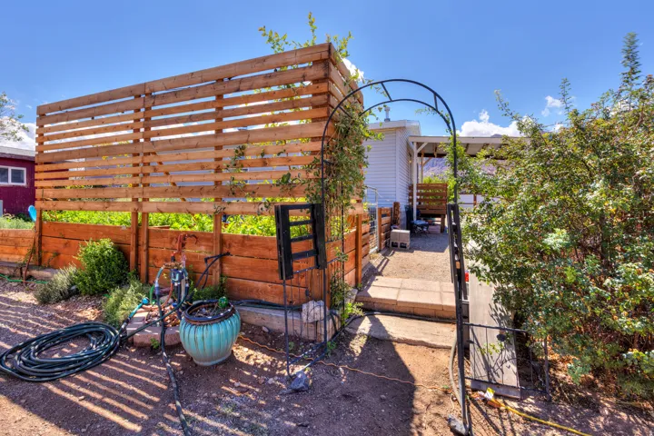 Wood slat privacy screen, raised garden beds, metal garden archway, paved pathway, and mature landscaping