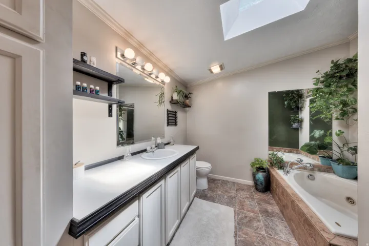 Dual vanity with an integrated sink, broad wall mirror, overhead vanity lighting, and a jetted soaking tub