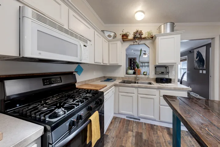 Kitchen featuring light-toned cabinetry, a black gas range, an integrated microwave, a double basin sink, and wood-finish flooring