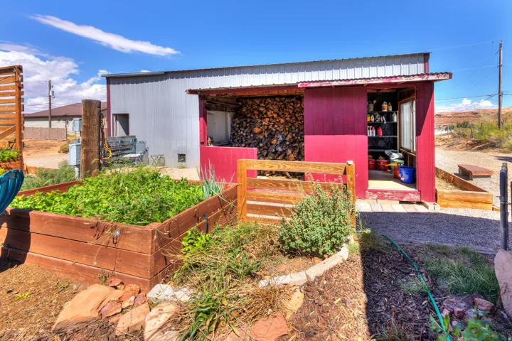 Raised garden beds, gravel hardscaping, red-painted shed, covered wood storage area, and a corrugated metal roof