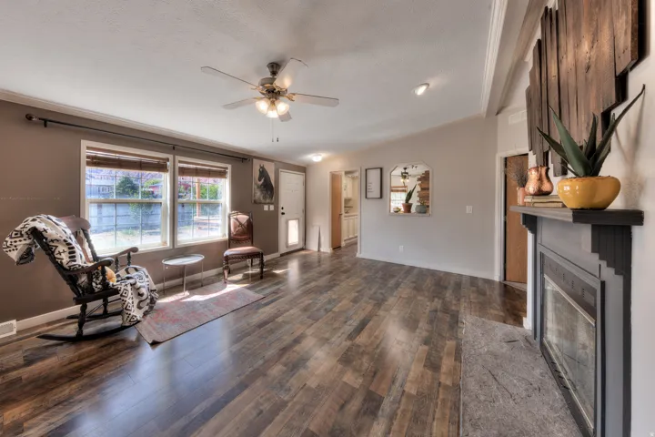 Spacious living area featuring wood-finish flooring, a fireplace with a mantel, multiple windows, and a ceiling fan