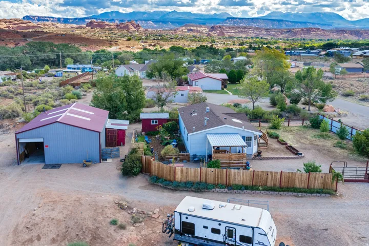 Expansive property featuring a detached metal-sided outbuilding with a roll-up door, a covered porch, wood fencing, and a gravel driveway