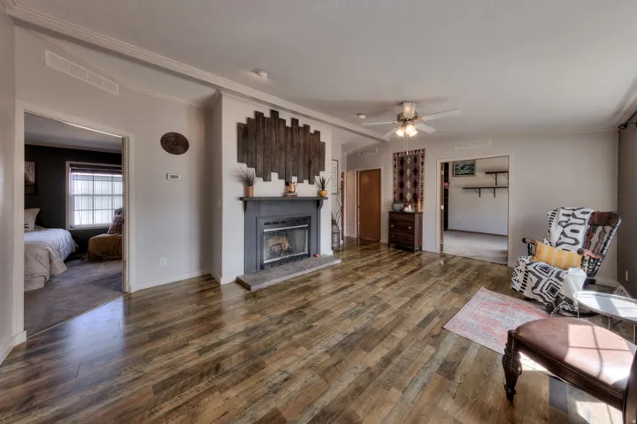 Wood-finish flooring throughout, fireplace with a mantle and stone hearth, crown molding, ceiling fan, and recessed lighting