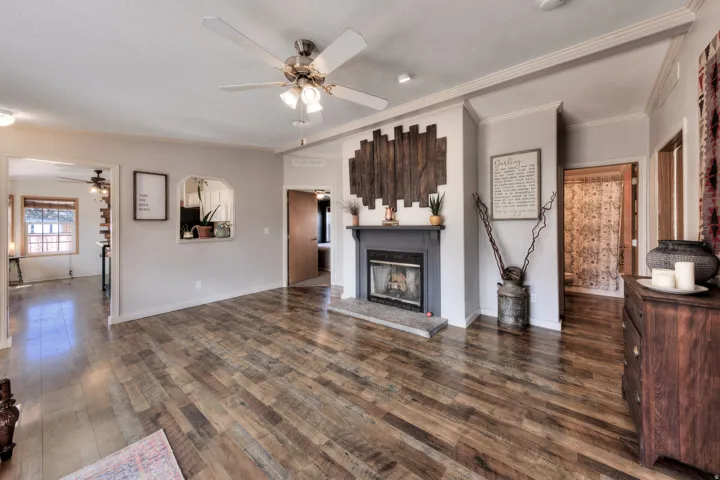 Wood-finish flooring throughout, ceiling fan with integrated lighting, fireplace with mantel and hearth, arched wall opening, and crown molding